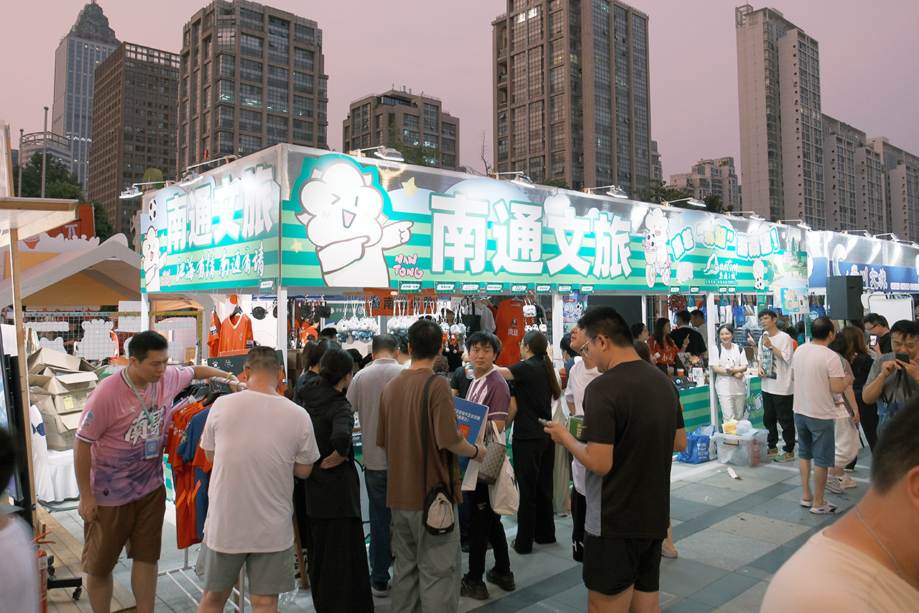 圖2：南通文旅攤位，「通通」蘇超玩偶、狼狼玩偶，藍(lán)印花布蘇小狼等南通好物吸引球迷觀眾排隊(duì)購(gòu)買。.jpg